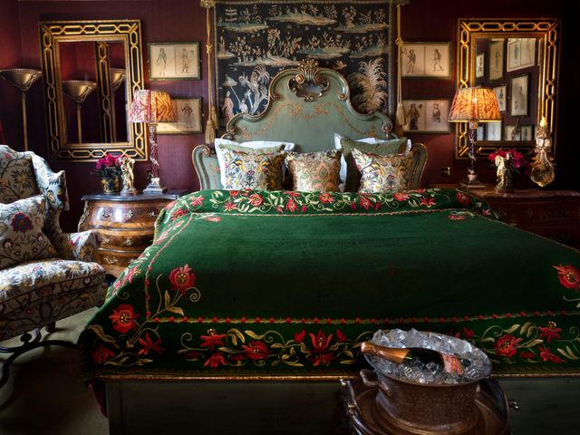 A regal looking hotel room with a dramatic bed with dark green blanket, print furnishings, mirrors and dark wallpaper at Prestonfield House.