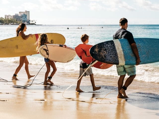 A family of four is seen holding surf boards on the beach as part of a surfing lesson while staying at the Twin Fin Hotel.