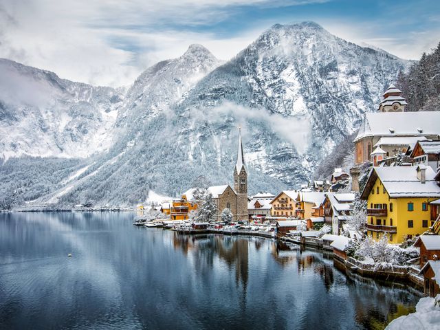 A lakefront town with Bavarian-style architecture covered in snow next to mountains.