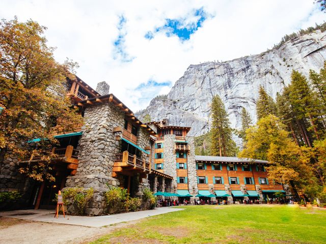 The exterior of The Ahwahnee with stone, wood, and turquoise accents in front of a large mountain bluff.