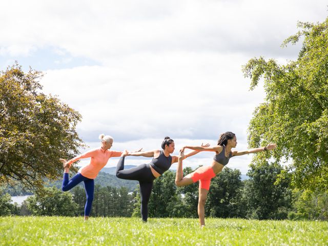 Three people perform yoga outdoors in a grassy area between trees at Kripalu.