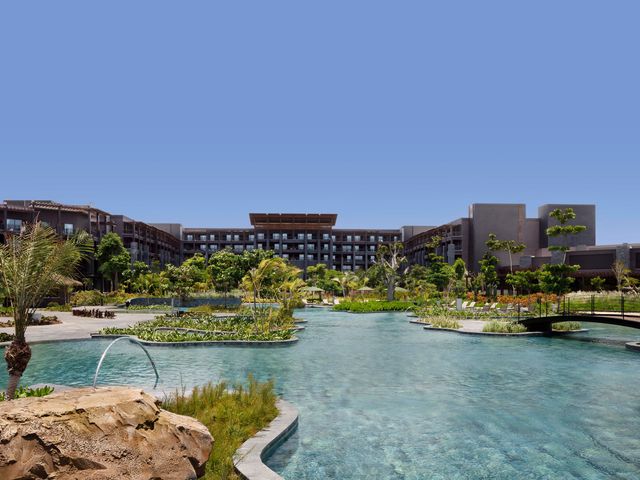 The grey exterior of Lopesan Caoba Lagoon Resort, Spa & Casino with balconies facing a lagoon-style pool.