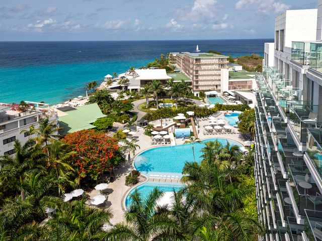 An aerial view over the Sonesta Resort in St. Maarten with multiple buildings, leafy trees, and hotel room balconies visible.