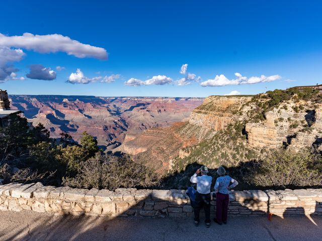 Two people standing next to a stone wall overlooking the edge of the Grand Canyon.