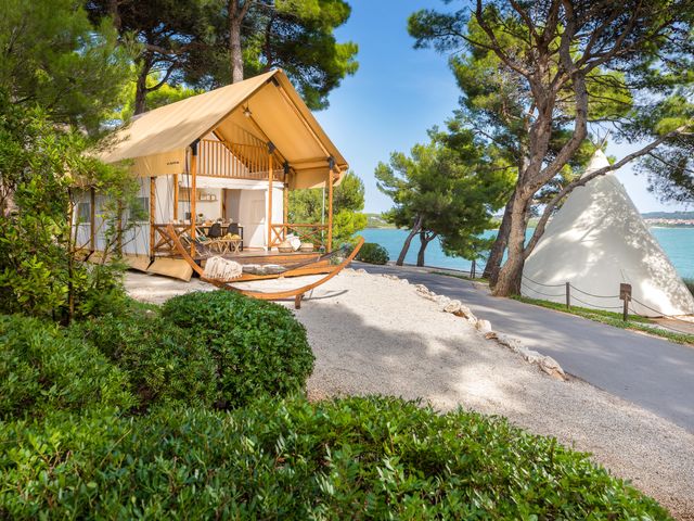 A white and beige tent with a hammock outside near the sea.