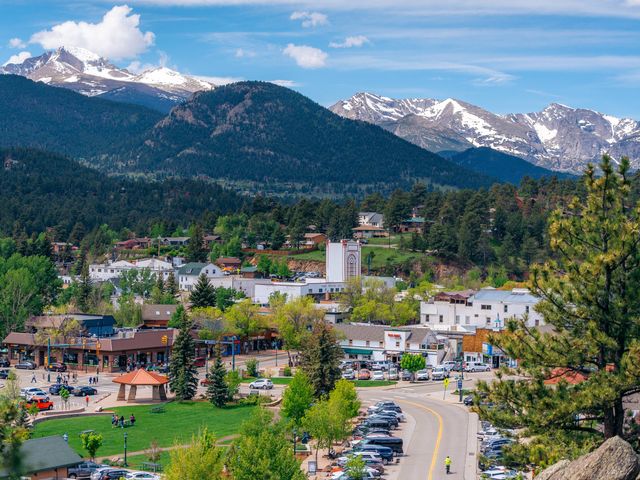 A panoramic view of Estes Park, Colorado with town buildings in the center surrounded by pine trees and mountain scenery.