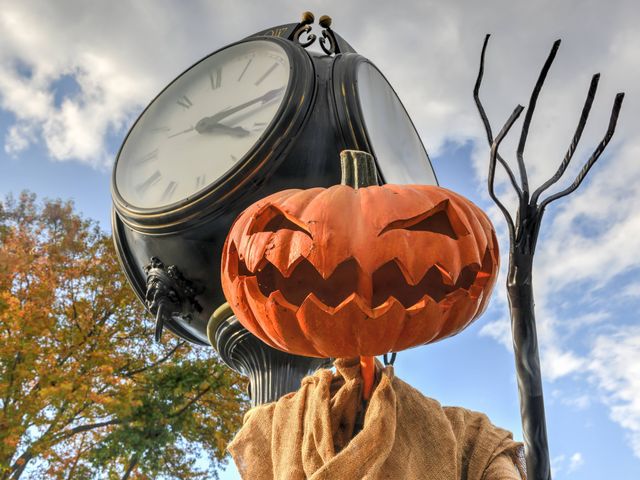 A jack-o'-lantern pumpkin is perched on something like a head next to a light post in Sleepy Hollow.