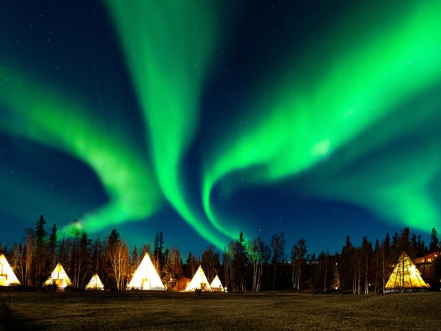 Green northern lights seen in a night sky over Yellowknife, Canada with lit-up tents.