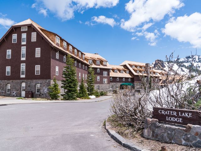 The exterior of Crater Lake Lodge, a large red and stone building next to snowy mountains.