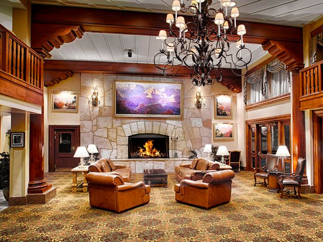 A rustic hotel lobby area with a fireplace, leather arm chairs, a chandelier, and balcony railings from the area above.