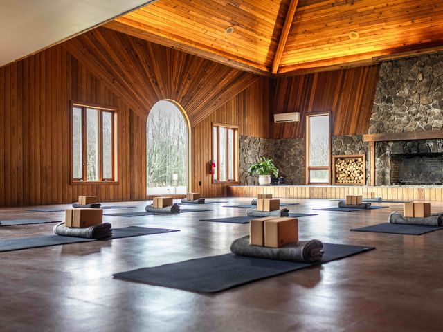 An empty movement studio with wood walls and a stone fireplace with mats set up on the floor at Hemlock Neversink. 