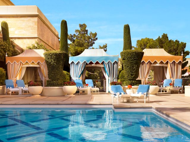 A pool with manicured hedges and orange and blue stylish cabanas.