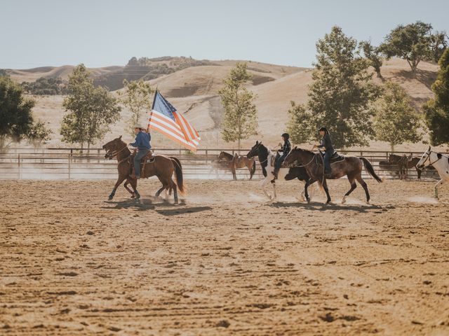 A man on a horse carrying an American flag leads other horse riders in a pen.