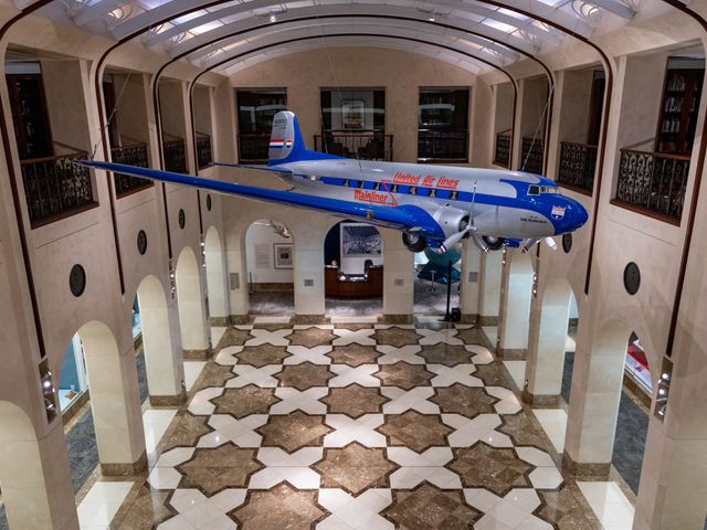 A model airplane is suspended from the ceiling over a tiled hallway.