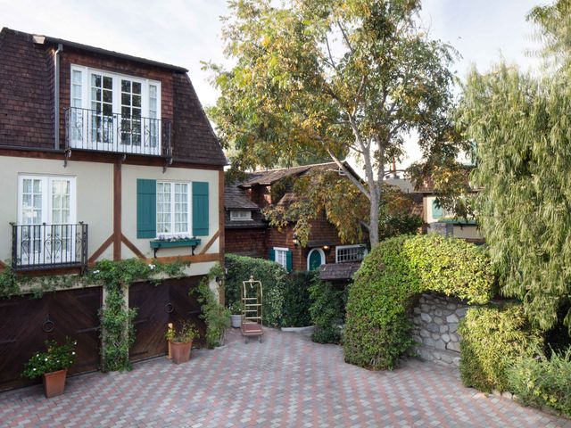 A hotel courtyard area surrounded by Tudor-style buildings, large trees, and manicured hedges.