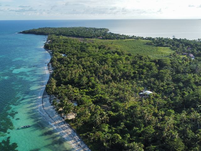 An aerial view over the dense, lush vegetation of Little Corn Island with turquoise water and reefs visible.