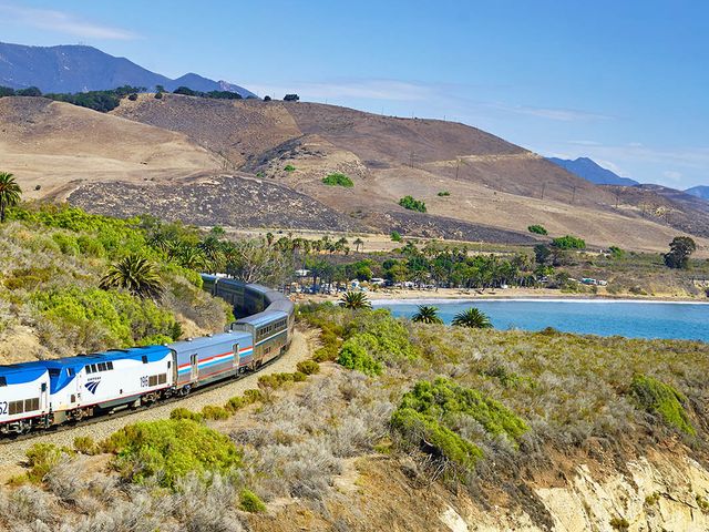 An Amtrak Coast Starlight train on the tracks next to the ocean in a scenic part of California.