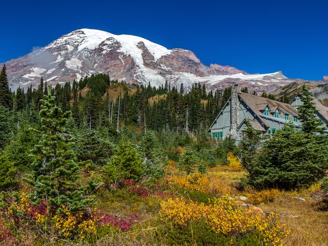 A grand mountain range surrounded by lush trees and flowers and a blue lodge building.