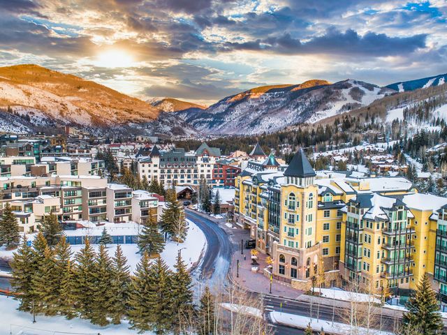 An aerial view over condos and lodge-style buildings in Vail with snowy mountains in the distance behind it.
