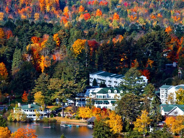 A collection of white buildings with green roofs next to a lake surrounded by fall foliage trees.