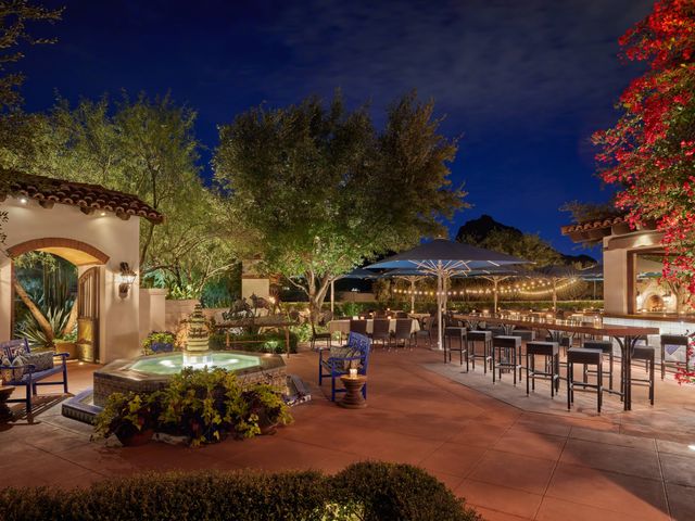 A patio at the El Chorro restaurant in Scottsdale at night with outdoor seating, a fountain, blue accents, and pink bougainvillea flowers.
