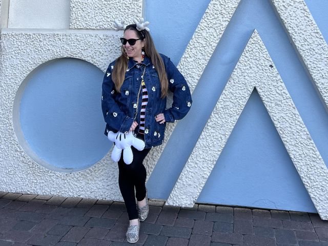 A woman poses for a photo with Mickey hand accessories while wearing a denim jacket.