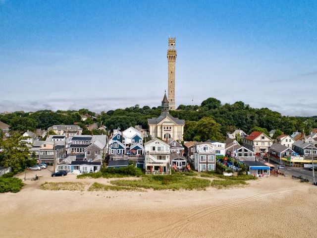 An aerial view of the coastline of Provincetown as seen from over the water with the Pilgrim Monument in the back of the skyline.