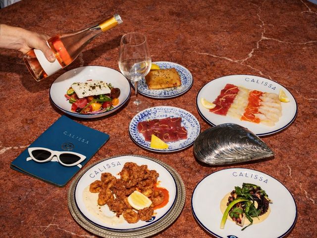 A hand pouring a glass of rose next to plates of food that say Calissa.