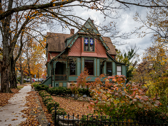 A small Victorian-style house with trees and bushes around changing color in fall.