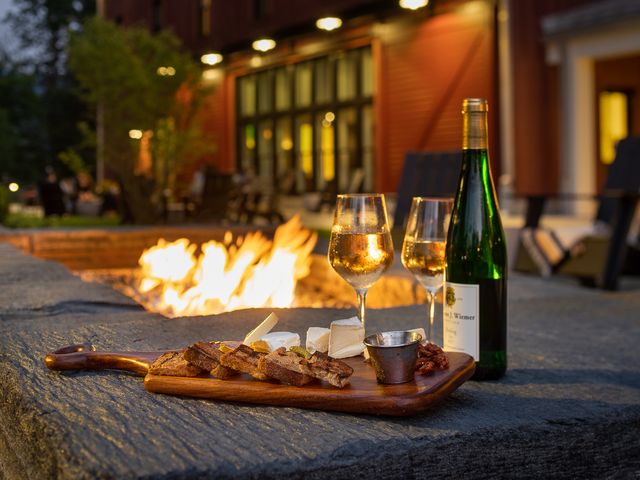 An outdoor firepit with a cheeseboard sitting on the edge and a wine bottle and two glasses.