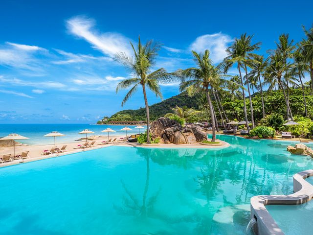 A pool facing a beach with chairs and umbrellas and palm trees at Sheraton Samui Resort.