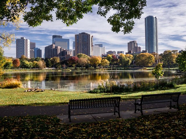 The Minneapolis skyline, as seen from a park with benches overlooking the view and a lake with fall foliage.
