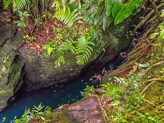 A look inside Titou Gorge, a slot canyon where visitors may float in Dominica, with people inside the water and lush canyon walls on either side.