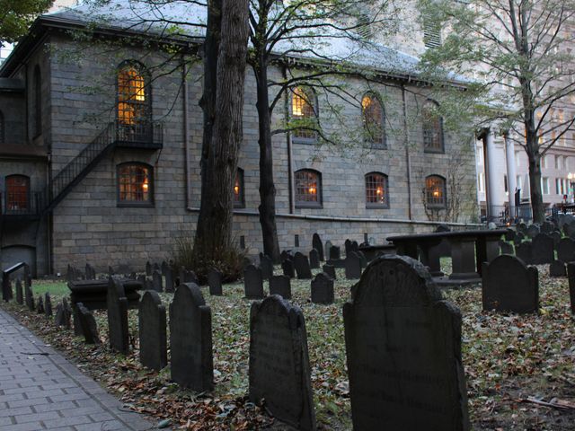 A historic church with rows of gravestones in a cemetery outside in Salem, MA.