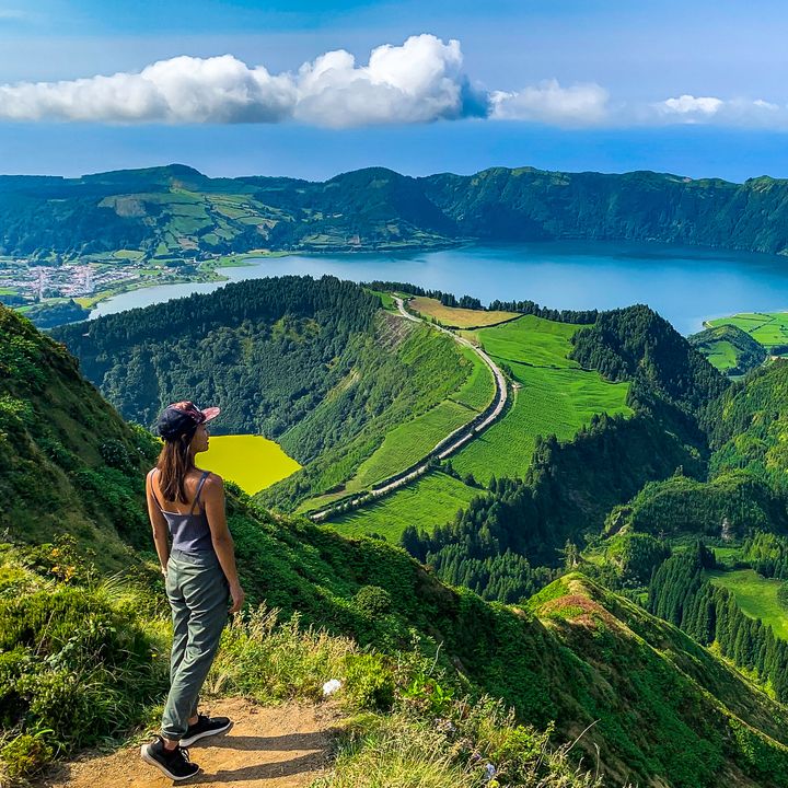 A woman standing at the edge of a hiking trail overlooking the Sete Cidades on Sao Miguel Island in the Azores.