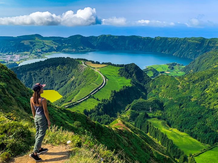 A woman standing at the edge of a hiking trail overlooking the Sete Cidades on Sao Miguel Island in the Azores.