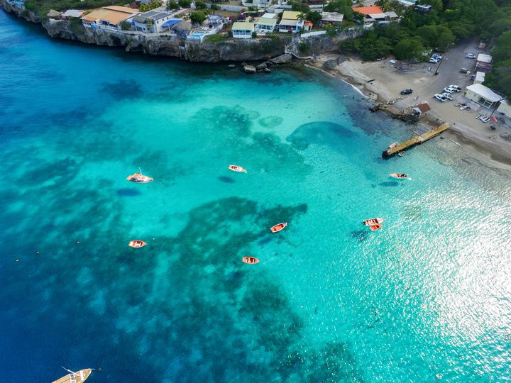 An aerial view over Westpunt in Curacao with its turquoise, blue clear waters alongside a small shore area,.
