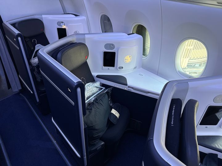 A business class window seat on a cabin on an Air France flight with a hanger and a pillow on the seat.