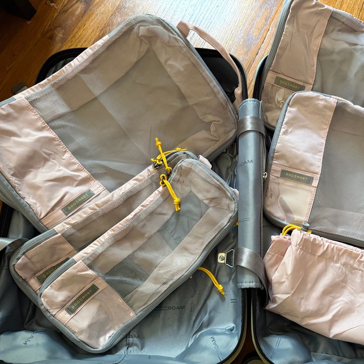 An empty suitcase with four packing cubes laid on top plus a matching drawstring pouch.