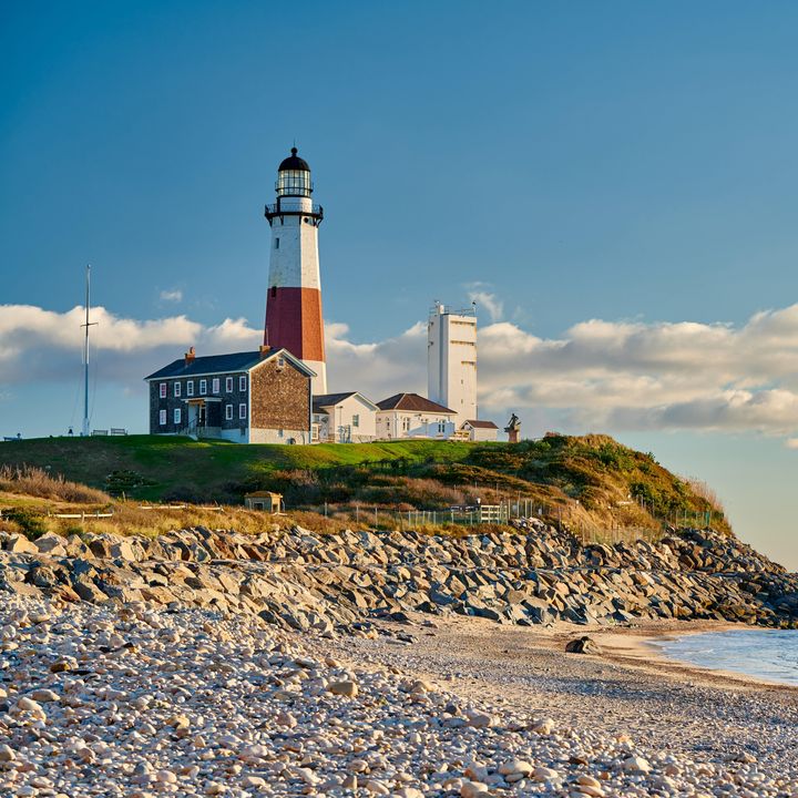 The Montauk Lighthouse next to a sandy beach with some rocks and grass on Long Island.