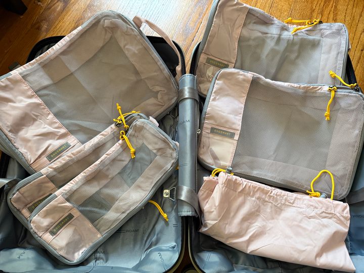 An empty suitcase with four packing cubes laid on top plus a matching drawstring pouch.