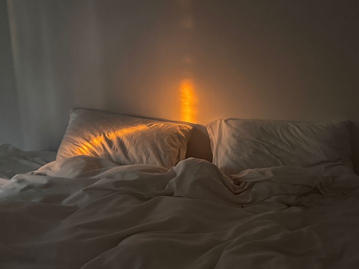 A bed with two white pillows and a white duvet with a sliver of golden sunlight spilling in.