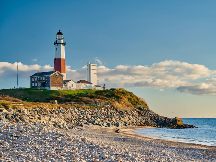 The Montauk Lighthouse next to a sandy beach with some rocks and grass on Long Island.