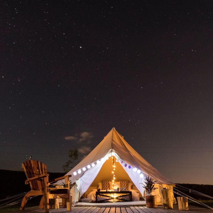 A glamping tent on a deck with an Adirondack chair under a starry night sky.