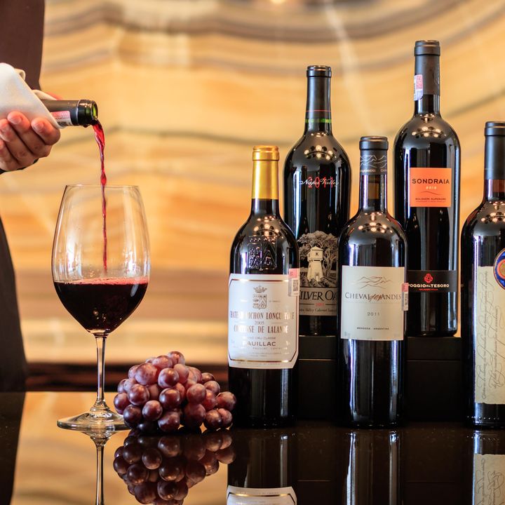 A hand is seen pouring a glass of wine next to a group of bottles.