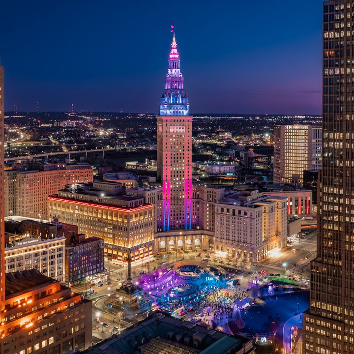 Buildings in Cleveland lit up at night, including a central skyscraper with colorful neon lights.