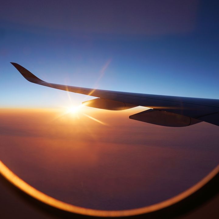 Sunlight peeking out from the clouds is seen through airplane window under the wing during sunrise.