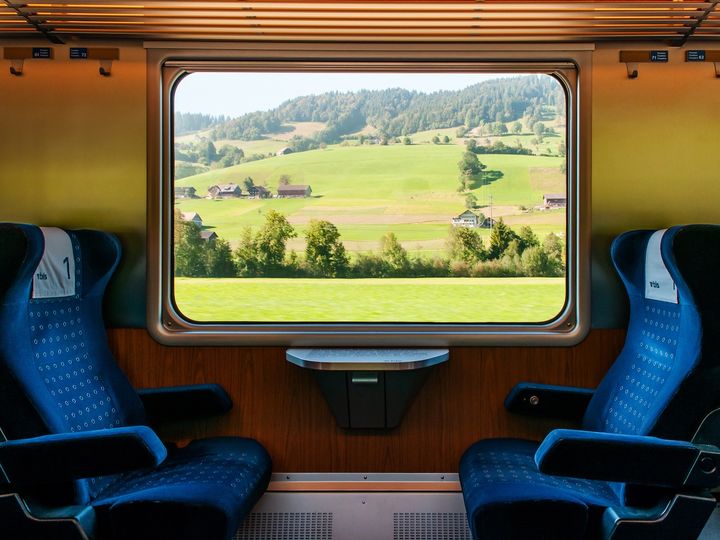 An interior view of a train car with two blue chairs facing each other and a rural scene out of the window.