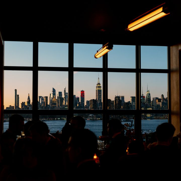 A bar with a large window overlooking the Manhattan skyline at dusk