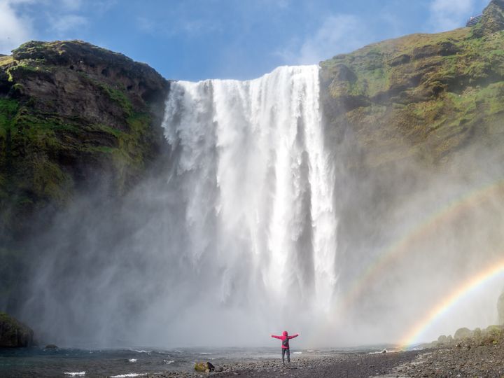 Person standing at foot of cascading waterfall with double rainbow